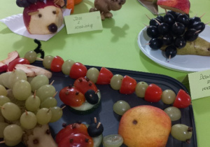 Na tacy są : jeż, gąsienica, biedronka i żółw z owoców i warzyw. Dalej widać tygrysa dwa jeżyki, sowę i żółte myszki też z owoców i warzyw.