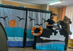 Sceneria morska, na kole ratunkowym napis Batory, Poland. Mężczyzna i kobieta przebrani za żołnierzy pomiędzy nimi postać niedźwiedzia Wojtka.