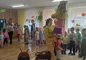 Przedszkolaki tańczą w kole pośrodku nauczycielka trzymająca Marzannę.
