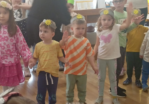 Dzieci w opaskach z emblematem słońca na głowie machają ręką.