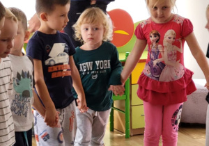 Mężczyzna w okularach stoi za dziećmi, które trzymają się za ręce.