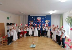 Grupa 5-latków z panią Bogusią pozuje w odświętnych strojach na tle pięknej, tematycznej dekoracji.