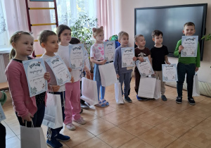 Wszystkie dzieci biorące udział w konkursie pozują do zdjęcia, trzymaja w dłoniach swoje nagrody i dyplomy.