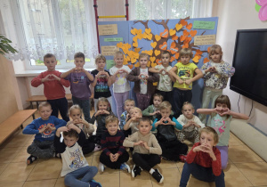 Grupa Motylków pozuje na tle drzewa tolerancji pełnego pomarańczowych serduszek zawieszonych przez wszystkie grupy.