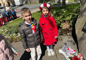Gabryś i Oktawia składają kwiaty pod pomnikiem.