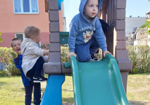 Chłopiec siedzi na zjeżdżalni. Drugi chłopiec wchodzi na zjeżdżalnię po stopniach.
