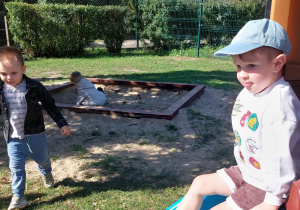 Trzech chłopców w ogrodzie przedszkolnym.Jeden siedzi na zjeżdżalni, drugi do niego idzie, a trzeci bawi się w piaskownicy.