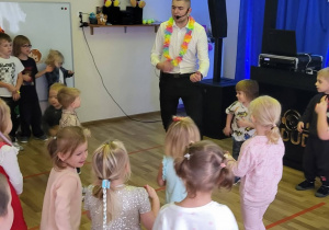 Didżej z girlandą na szyi, przed nim tańczące dzieci.
