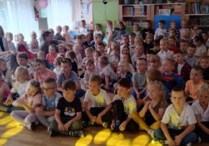 Przedszkolaki siedzą na podłodze w oczekiwaniu na zabawę.