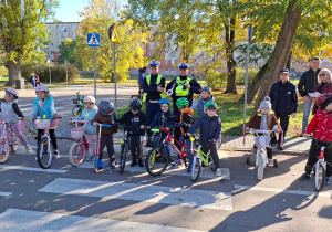 Dzieci siedzą na rowerach za nimi stoją policjanci i rodzice oraz pani dyrektor.