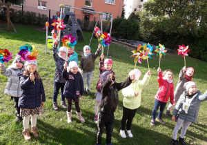 Dzieci z grupy 5-latków obserwują siłę wiatru, który wprowadza w ruch wiatrakiw ogrodzie przedszkolnym