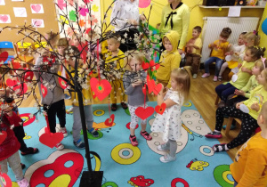 Dzieci dekorują Drzewo Życzliwości samodzielnie wykonanymi serduszkami i buźkami