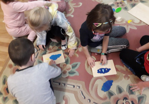 6-latki siedzą na dywanie i układają drewniane puzzle "Zjawiska pogodowe".