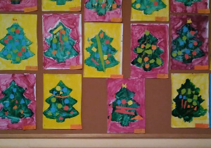 Tablica prac plastycznych 5-latków. Na niej zawieszone prace dzieci-choinki udekorowane wyciętymi z kolorowego papieru bombkami, według własnego pomysłu.