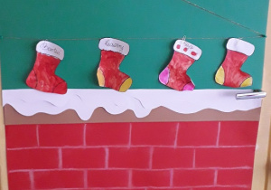 Nad kominkiem wykonanym z brystolu, wiszą pomalowane przez dzieci czerwone skarpety na prezenty.