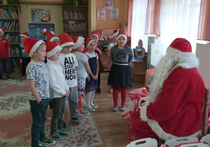 6-latki w czerwonych czapkach otrzymują od Mikołaja prezenty.
