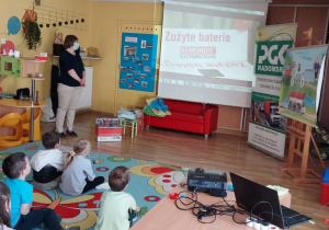Starszaki podczas warsztatów oglądają film o segregowaniu odpadów. Pracownik PGK Radomsko wyjaśnia dzieciom, co należy zrobić ze zużytymi bateriami.