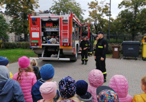 Dzieci uważnie słuchają o tym, co mówią o swojej pracy strażacy.