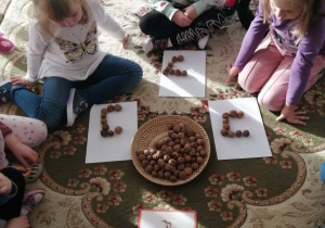 Dziewczynki z grupy PROMYCZKÓW układają obraz graficzny litery „i” za pomocą orzechów.