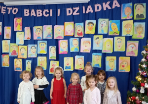 Dziewczynki z grupy 4-latków na tle portretów Babć i Dziadziusiów.