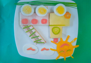 Kanapka w kształcie samochodu ciężarowego z podniesioną drabiną, w górze serowe słoneczko i chmurki z białego sera.