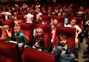 Dzieci z grupy pięciolatków siedzą w fotelach na widowni sali teatralnej.