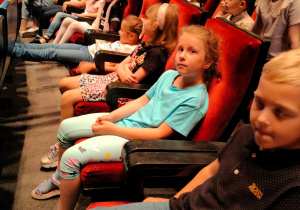 Dzieci z grupy sześciolatków siedzą w fotelach na widowni sali teatralnej.
