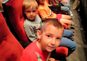 Chłopcy z grupy sześciolatków siedzą w fotelach na widowni sali teatralnej.