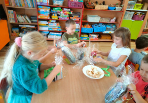Hania, Nikodem, Lila i Olek z zapałem rozpakowują przy stoliku swoje prezenty.