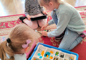 Lilianna, maja i Julia budują roboty z klocków lego, według instrukcji podanej na tablecie.