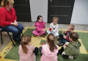 Dzieci siedzą na dywanie i podają sobie mikołajkową maskotkę.