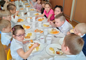 Na zdjęciu dzieci jedzą drugie danie (ziemniaki, rybę i surówkę), podczas wigilijnego spotkania.