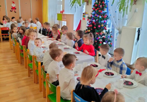 Dzieci, odświętnie ubrane, podczas wigilijnego spotkania w przedszkolu jedzą postny barszczyk z uszkami.
