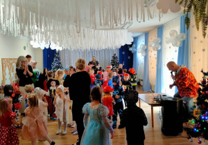 W pięknej, zimowej scenerii, przedszkolaki w kolorowych strojach tańczą przy muzyce zaproponowanej przez Pana Wodzireja.