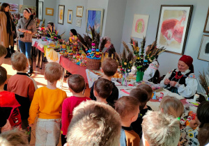 Dzieci oglądają kolorowe rękodzieła, prezentowane przez twórczynie ludowe z regionu opoczyńskiego.
