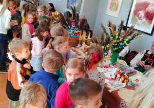 Dzieci oglądają kolorowe rękodzieła, prezentowane przez twórczynie ludowe z regionu opoczyńskiego.