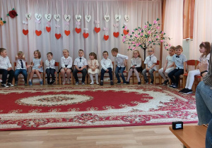 Grupa Słoneczka siedzi w półkolu, w oczekiwaniu na rodziców, gotowa do występu okolicznościowego.
