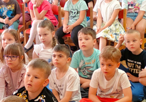 Przedszkolaki siedzą na dywanie i słuchają opowiadania autorstwa pani Elżbiety Stępień.