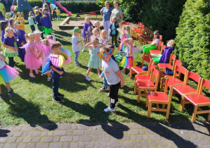 Kolorowe przedszkolaki bawią się i tańczą wesoło na placu przedszkolnym.