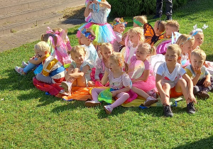 Przedszkolaki z grupy Motylki siedzą na kolorowej chuście w ogrodzie przedszkolnym.