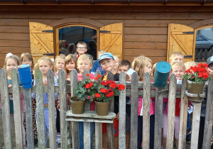 Dzieci z grupy Jagódki stoją za drewnianym płotkiem.