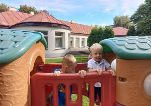 Dwóch chłopców stoi za barierką lokomotywy - zabawki w ogrodzie przedszkolnym.