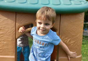 Uśmiechnięty chłopiec stoi w drzwiach lokomotywy - zabawki ogrodowej.