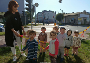 Dzieci z nauczycielką podczas spaceru ulicą Tysiąclecia. W tle sygnalizacja na skrzyżowaniu.