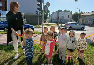 Dzieci z nauczycielką podczas spaceru ulicą Tysiąclecia. W tle sygnalizacja na skrzyżowaniu.