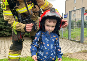 Strażak zakłada chłopcu kask strażacki.