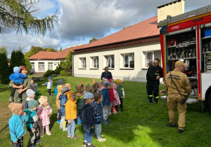 Dzieci stoją przed wozem strażackim i oglądają przyrządy jakimi dysponują strażacy w swojej pracy.