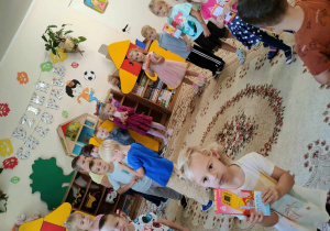 Dzieci z grupy Motylki stoją w kole na dywanie. Dziewczynki wręczają chłopcom prezenty-gry.