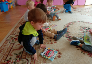Dzieci z grupy Słoneczka siedzą na dywanie i oglądają prezenty-książeczki zatytułowane Wóz strażacki.