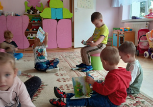 Dzieci z grupy Słoneczka siedzą na dywanie i oglądają prezenty-książeczki zatytułowane Wóz strażacki.